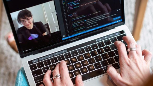 Person coding on a laptop during a video conference, showcasing remote work.