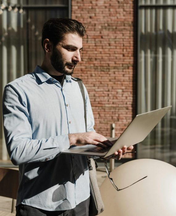 Bearded man in blue shirt using laptop outdoors, remote work concept.